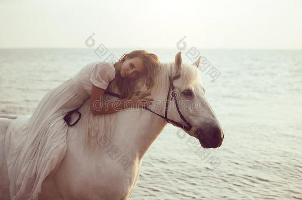 穿着白色连衣裙的女孩在海滩上骑着马