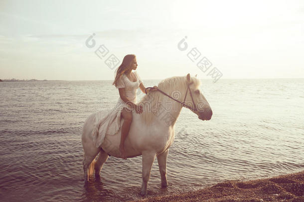 穿<strong>着</strong>白色连衣裙的女孩在海滩上<strong>骑着马</strong>