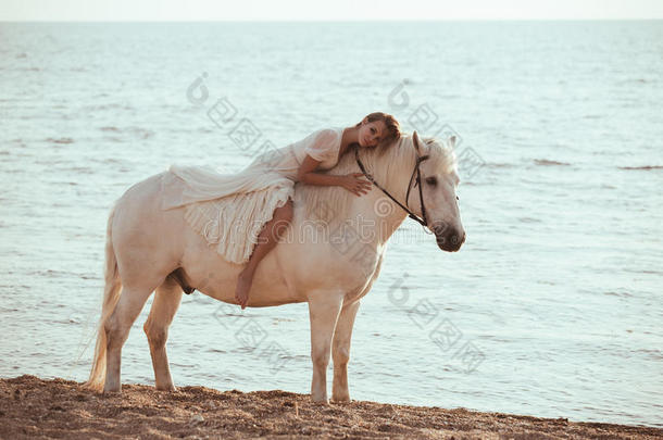 穿着白色连衣裙的女孩在海滩上骑着马