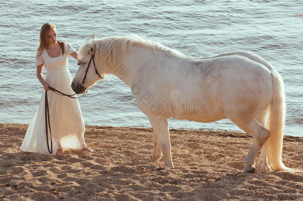 穿<strong>着</strong>白色连衣裙的女孩在海滩上<strong>骑着马</strong>