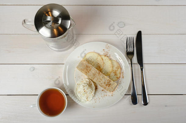 一片苹果丝，一杯茶，茶壶和白色木制桌子上的餐具。 顶级威夫。
