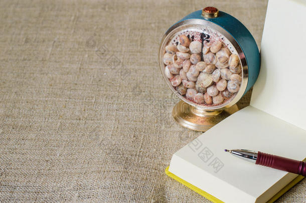 一个开放的迷你记事本与笔和一个工艺钟与贝壳。