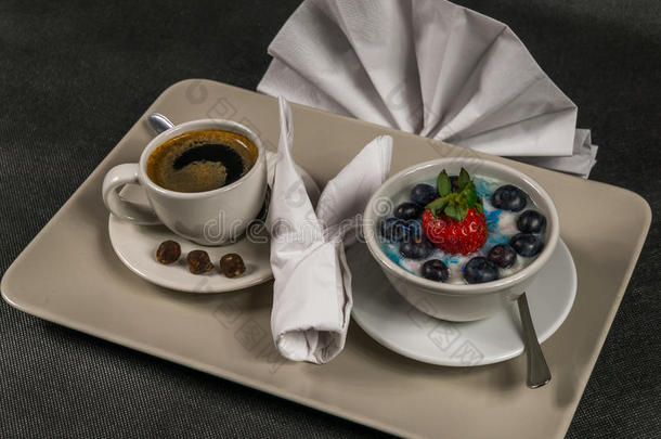 黑色咖啡在奶油杯，甜点，酸奶与大草莓和蓝莓，在灰色盘子，餐巾纸