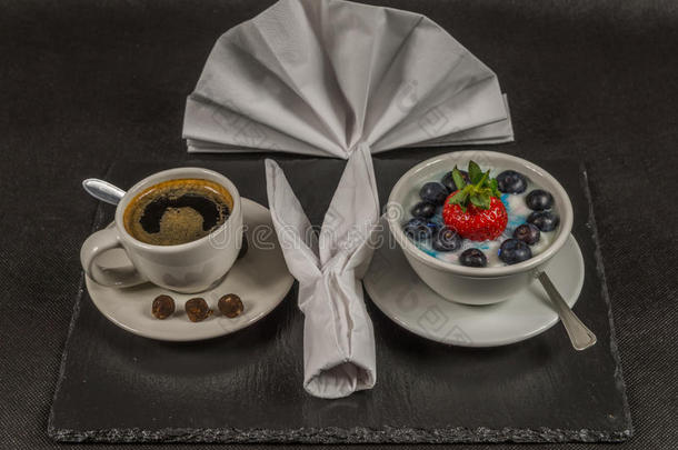 白色杯子里的<strong>黑色</strong>咖啡，甜点，大草莓和蓝莓的酸奶，在<strong>黑色</strong>的<strong>石板</strong>上，餐巾纸