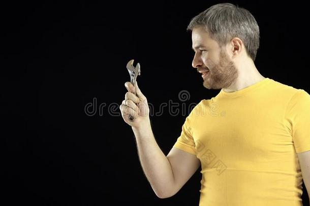穿着黄色T恤的开朗男人拿着可调节的扳手。 DIY，维修，业余建筑或家庭改善概念