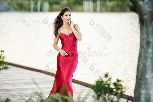 花园里漂亮的年轻女人穿着一件<strong>长长</strong>的丝绸红色连衣裙。