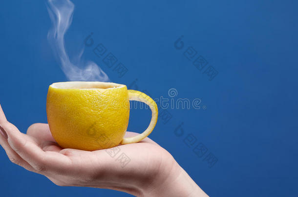 柠檬做的茶杯。 柠檬杯在手，蓝色背景。 天然水果茶主题的创意构图