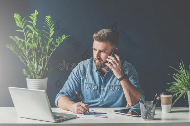 商人坐在办公室的桌子上，在手机上交谈，同时看着<strong>笔记</strong>本电脑屏幕和做<strong>笔记</strong>。
