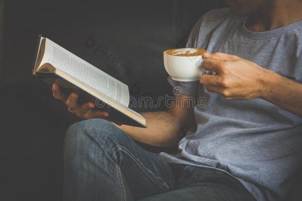 一个男人看书，端着一杯咖啡。