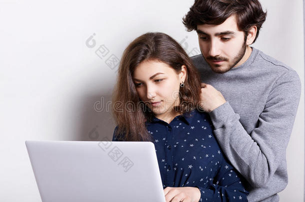 一个漂亮的学生帮她时髦的男朋友拿他的文凭纸。 一个时髦的人看着笔记本电脑上的演示，靠在她身上