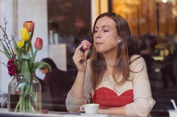美丽的年轻女人坐在靠近窗户的咖啡店里，喝咖啡，吃甜点