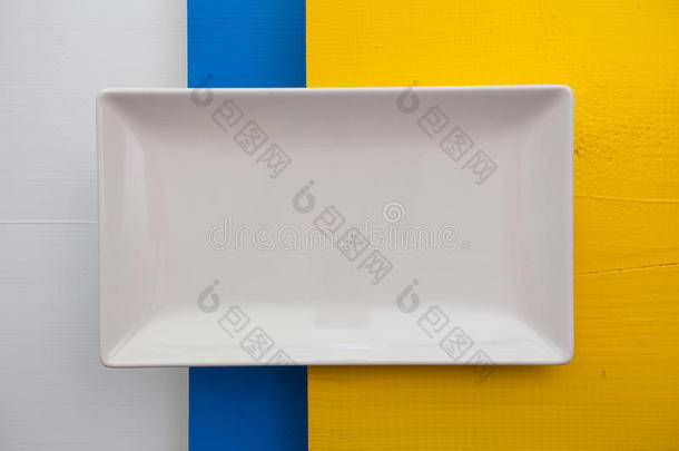 空的白色陶瓷盘在白色，蓝色和黄色的木制上