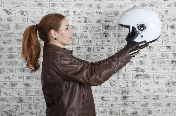 美丽的摩托车手选择白色开放头盔，同时保持伸展手臂，砖墙背景，侧视