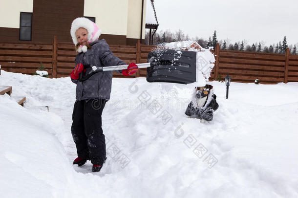 带着狗的女孩用铲子把雪从跑道上拿下来