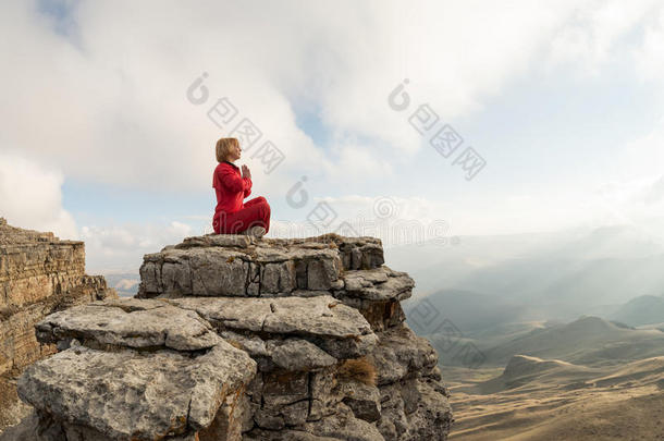 一个美丽的女孩在日落的背景下，坐在云层上方的岩石上，摆出莲花的姿势沉思