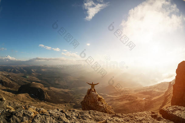 一个快乐的人，他的手高高地站在一个单独站立的岩石上，这是在云层之上对着云层