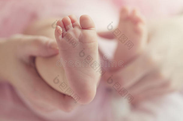 特写母亲的手，抱着可爱的小婴儿脚，展示婴儿的脚。 调色。 粉红色的背景。 水平的。