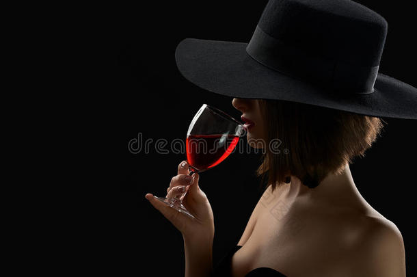 优雅神秘的女人戴着一顶帽子，戴着一杯红酒