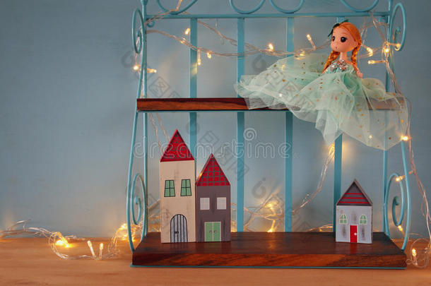 可爱的娃娃和木制的小房子旁边温暖的花环灯前面的蓝色背景。