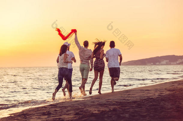 一群快乐的年轻人正在日落海滩和大海的背景下跑步