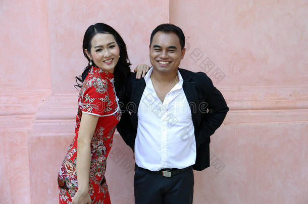 亚洲夫妇穿着<strong>中式</strong>连衣裙，微笑着站在一堵粉<strong>红色</strong>的墙上