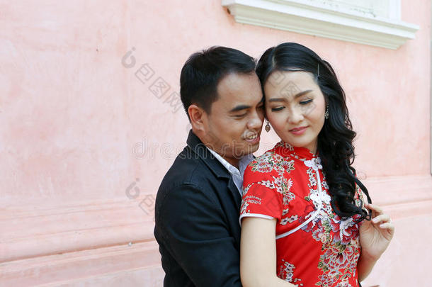 穿中式连衣裙的亚洲夫妇互相捧着一堵粉红色的墙