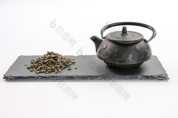 长方形页岩板上的铸铁黑茶壶和一把叶子绿茶