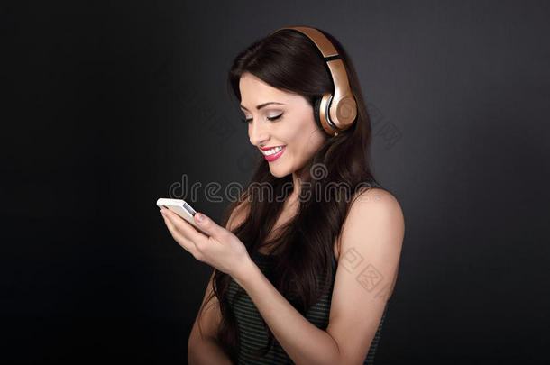 美丽平静的年轻女人从手机上听无线耳机里的音乐，在深灰色的背景上微笑