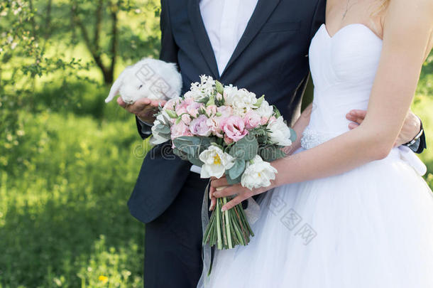 新娘手里拿着一束精致的婚礼花束，里面有白色和粉红色的郁金香和粉红色的小玫瑰。 新郎抱着一个白色的可爱