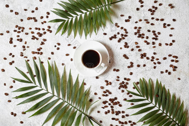 一杯黑色浓缩咖啡，在白色的混凝土背景上，有<strong>散落</strong>的<strong>咖啡豆</strong>和棕榈枝。 在温暖的地方休息