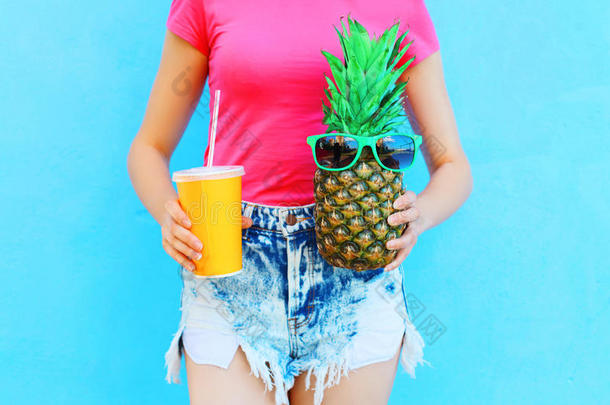 时尚女人手里拿着一杯果汁和菠萝，戴着五颜六色的太阳镜