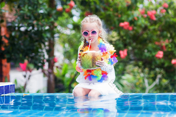 穿着粉红色泳装和太阳镜的漂亮女孩正在喝椰奶，看着相机，在游泳池里游泳时微笑