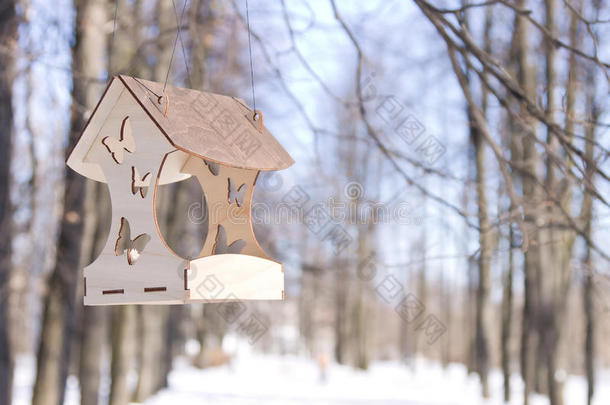 优雅的木制鸟类饲养器悬挂在冬季公园的树枝上