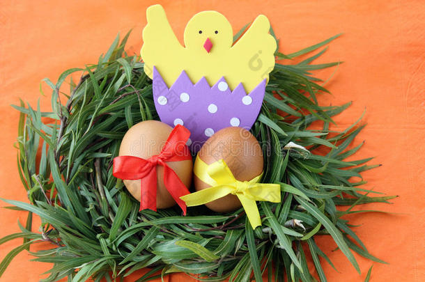 复活节装饰：黄色的鸡蛋和手工制作的蛋壳中孵化的小鸡在绿色的草枝巢在橙色的背景上