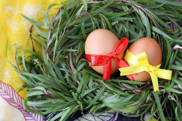 复活节装饰：两个黄色的鸡蛋，花边丝带在绿色的草枝巢在黄色的背景
