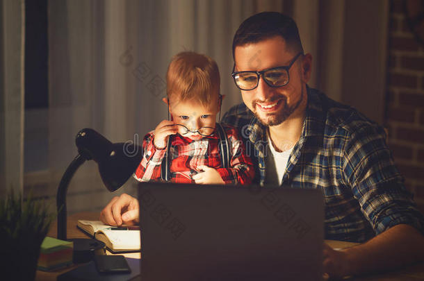 父亲和儿子婴儿在黑暗中在家电脑工作