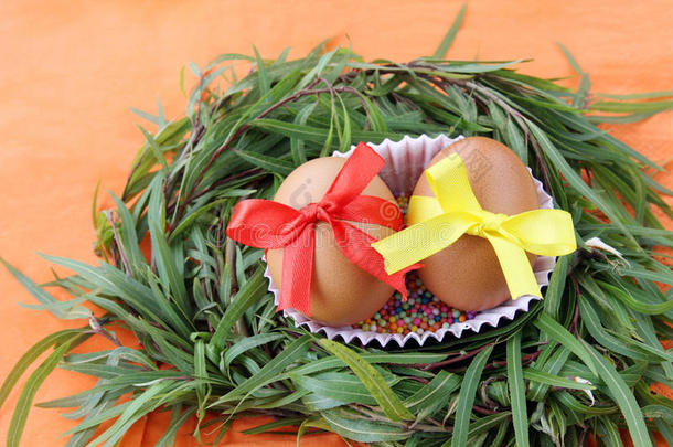 复活节装饰：两个黄色的鸡蛋，<strong>花边</strong>丝带在绿色的草枝巢在橙色的背景
