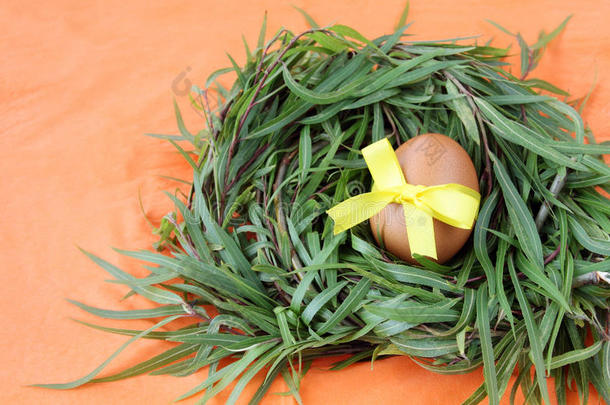 复活节装饰：黄色鸡蛋与花边丝带在绿色草枝巢在橙色背景