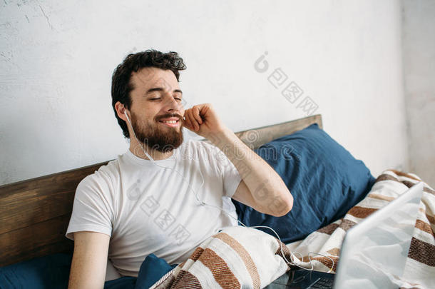 长胡子的男人躺在早上的床上拿着笔记本电脑