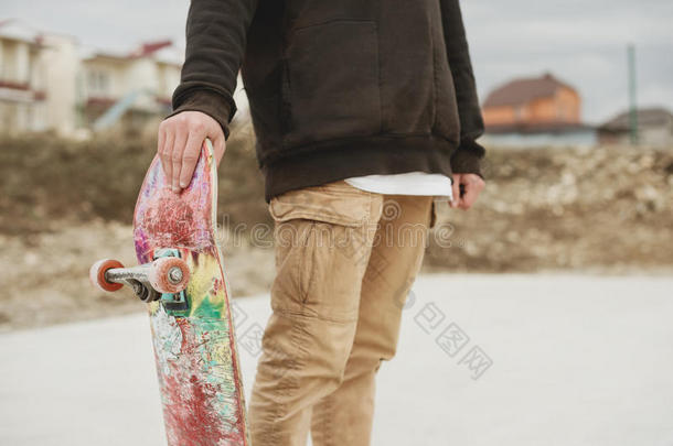 特写少年站在右侧帽衫，手持滑板在背景贫民窟