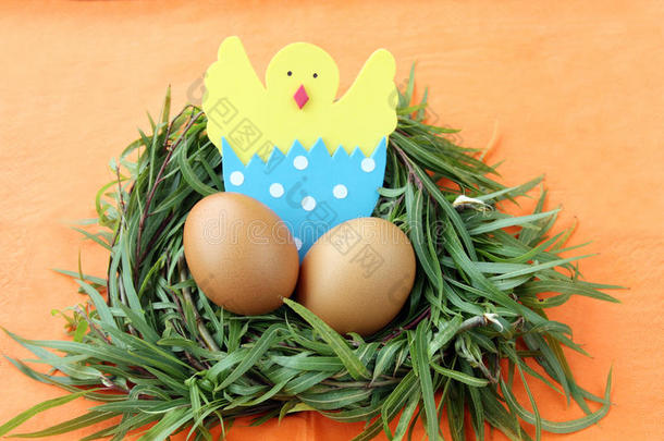 复活节装饰：黄色的鸡蛋和手工制作的蛋壳中<strong>孵化</strong>的<strong>小鸡</strong>在绿色的草枝巢在橙色的背景上