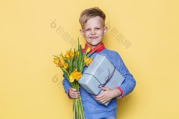 英俊的男孩拿着花束和<strong>礼品</strong>盒。 <strong>情人节</strong>`。 生日。 妈妈`一天。 黄色背景下的工作室肖像