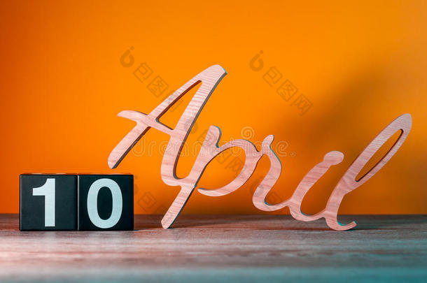 四月十日。 每月10日，每日木制日历在桌子上，橙色背景。 春季时间概念