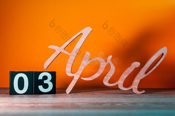 <strong>四月</strong>三日。 每月第三天，每日木制日历在桌子上，橙色背景。 春季时间概念