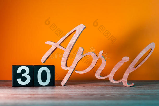 四月三十日。 每月30日，每日木制日历在桌子上，橙色背景。 春季时间概念