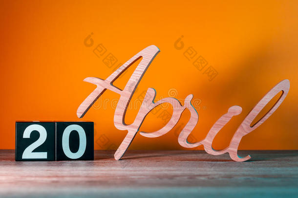 四月二十日。 每月20日，每日木制日历在桌子上，橙色背景。 春季时间概念