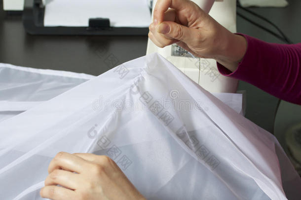 一个女人在缝纫机上工作。 她把窗帘缝在窗户上。