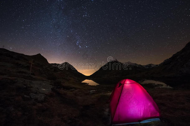 在星空下露营，在意大利法国阿尔卑斯山的高空上在银河弧下露营。 前景中发光的帐篷。 冒险