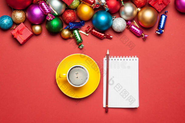 一杯咖啡，笔记本，铅笔和美丽的圣诞装饰在美妙的红色背景上