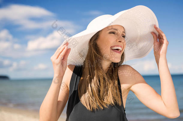 戴帽子的美女在海滩上笑着看着远方
